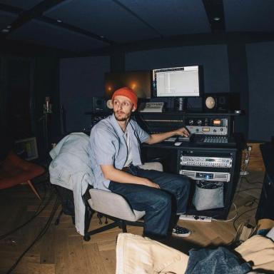 Chris sits at desk wearing an orange beanie hat, light blue shirt and navy jeans